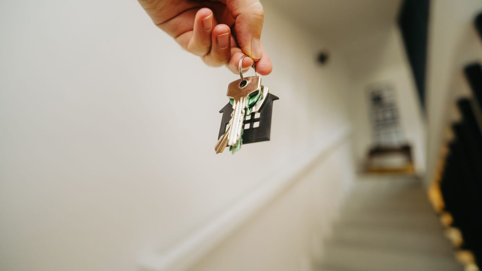 A hand holding a set of keys on a house-shaped keychain at the top of a staircase